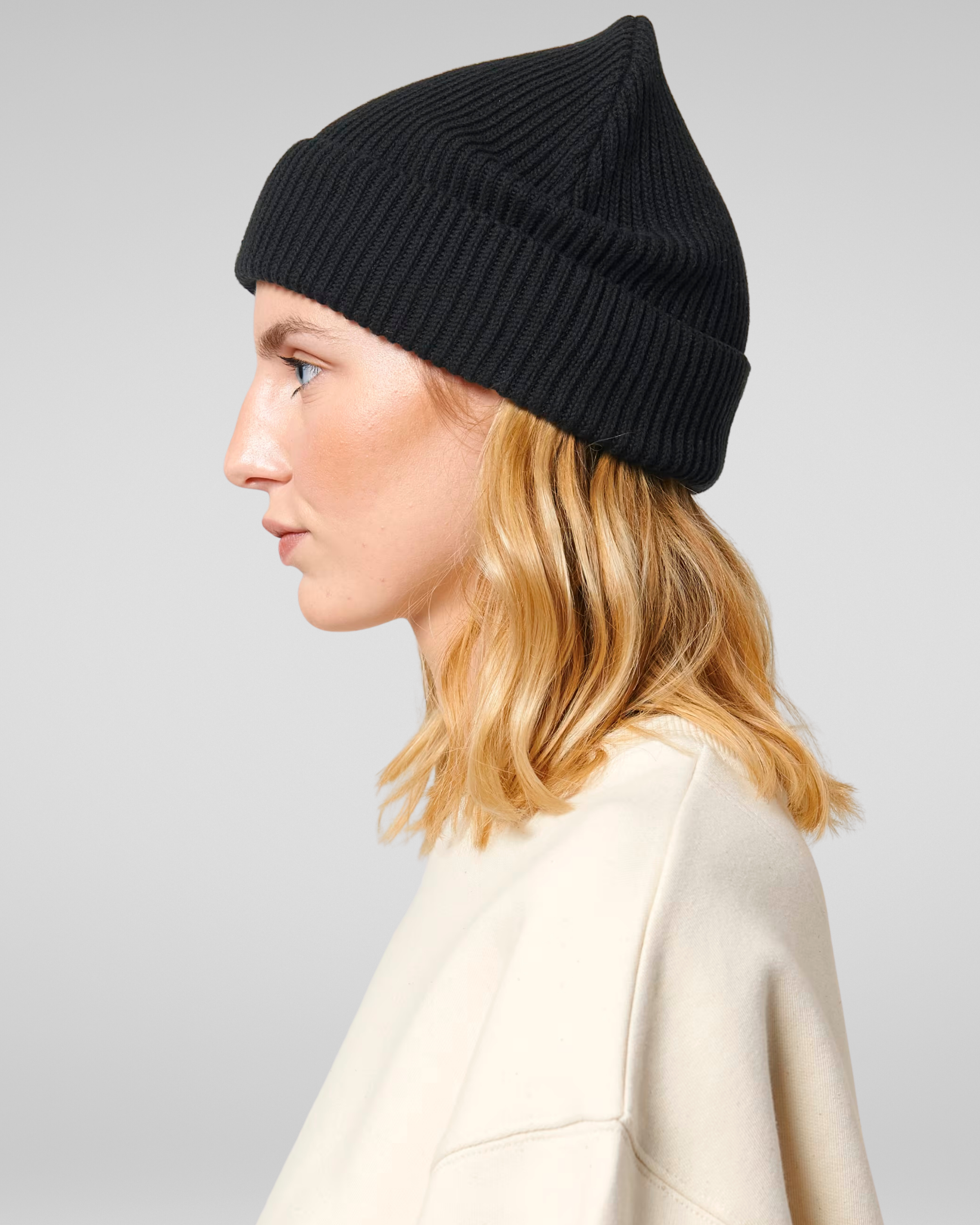 Person wearing a black beanie and beige coat on a gray background